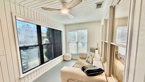 Ein geräumiges Zimmer mit großem Fenster, Deckenventilator und einer gemütlichen Sitzecke mit Sofa und Kissen.