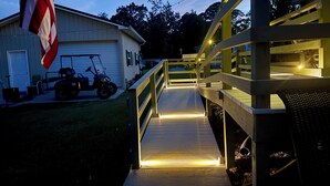 Eine Holterrasse mit Geländern führt zu einem Haus mit Garage, vor der ein Golfmobil geparkt ist.