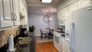 A kitchen with white cabinets, a black countertop, a clock on the wall, and a dining area with a table and chairs. - Tranquil 3-bedroom house with AC in Elk Grove Village (Elk Grove Village)