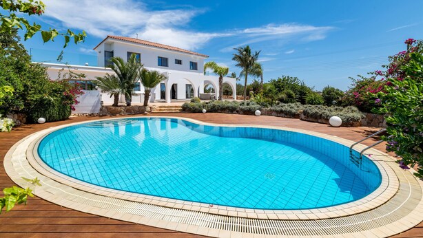 A swimming pool surrounded by a wooden deck, with a white building in the background. - Ayia Napa Panorama Villa (Ayia Napa)