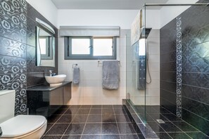 A modern bathroom with a glass shower enclosure, a vanity with a sink, and a toilet. - Ayia Napa Panorama Villa (Ayia Napa)