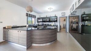 A modern kitchen with a curved island, stainless steel appliances, and a hanging light fixture. - Ayia Napa Panorama Villa (Ayia Napa)