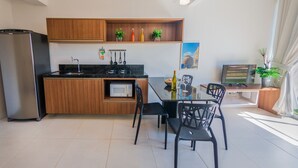 Una cuina moderna amb armaris de fusta, microones integrat i zona de menjador amb cadires negres i taula de vidre.