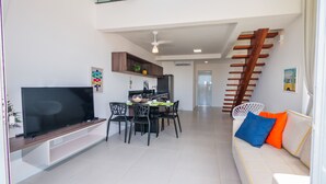 Un saló modern amb televisió plana, zona de menjador, escala i un sofà amb coixins.