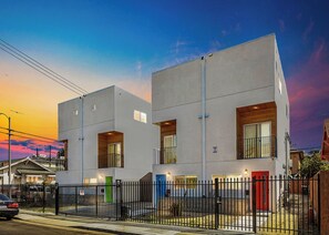 A modern two-story residential building with a flat roof, a black metal fence, and a red door. - Experience Luxury 4BR Townhouse, Sleeps 8 with Parking (Los Angeles)