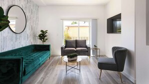 A modern living room with a green sofa, a black armchair, a coffee table, and a large window with a view of a balcony. - Experience Luxury 4BR Townhouse, Sleeps 8 with Parking (Los Angeles)