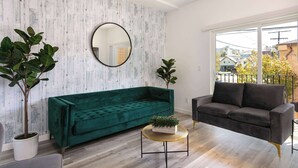 A living room with a green velvet sofa, a round mirror, and two potted plants. - Experience Luxury 4BR Townhouse, Sleeps 8 with Parking (Los Angeles)