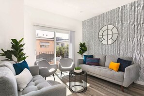 Un salon moderne avec un canapé gris, deux fauteuils, une table basse et un mur orné d’un motif.