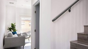 Un couloir moderne avec un canapé gris, une plante en pot et un escalier.