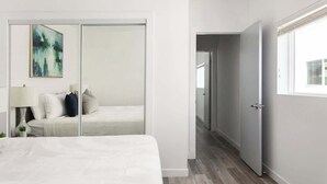 Une chambre à coucher moderne avec un lit, une table de chevet, une lampe, un miroir et un tableau.