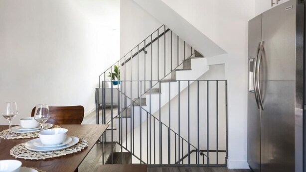 Une cuisine moderne avec un réfrigérateur en acier inoxydable, une table à manger dressée avec de l’assiette blanche et des verres à vin, et un escalier doté d’une rampe en métal.
