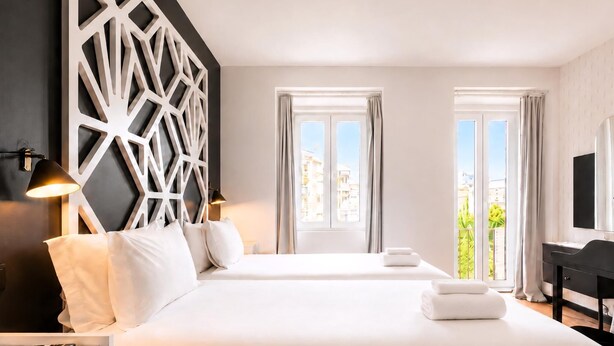 Una habitación de hotel con cama, mesitas de noche, un escritorio y un ventanal con cortinas.