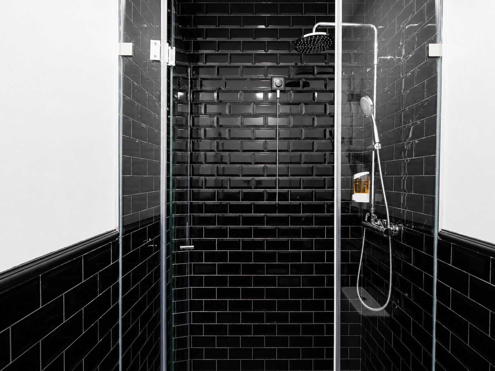 A modern shower with a glass enclosure, black tiled walls, and a handheld showerhead.