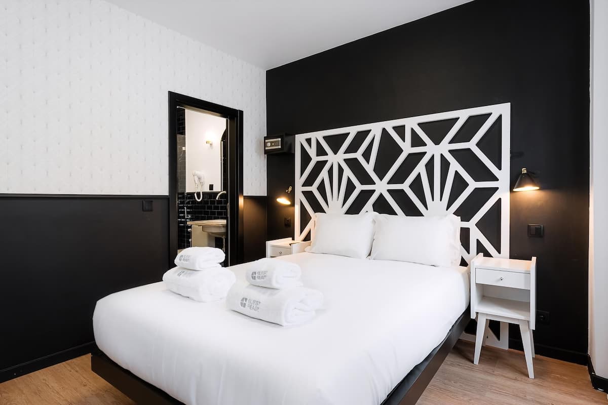 A modern hotel room with a black and white color scheme, a geometric headboard, a neatly made bed with towels, a bedside table, and a nightstand.