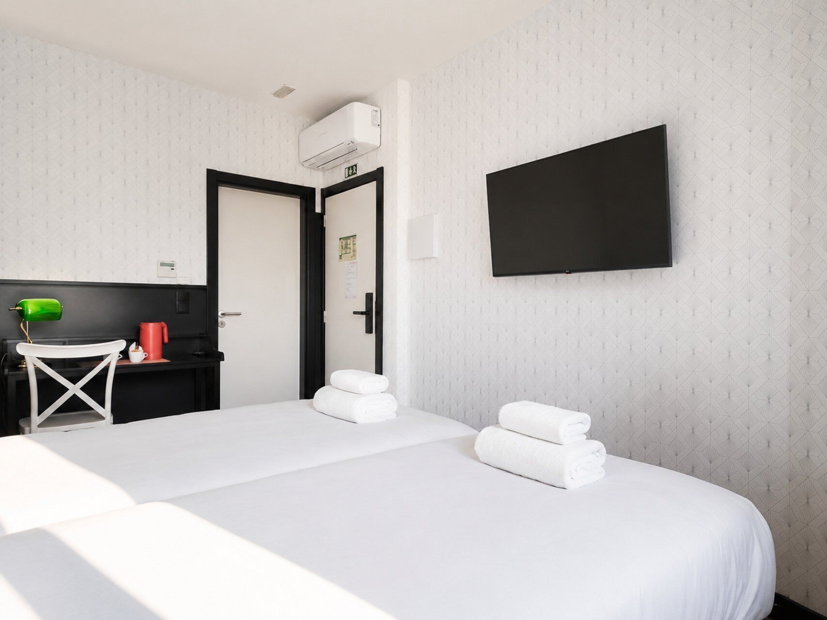 Een hotelkamer met een bed, een bureau met lamp, een televisie en een deur.