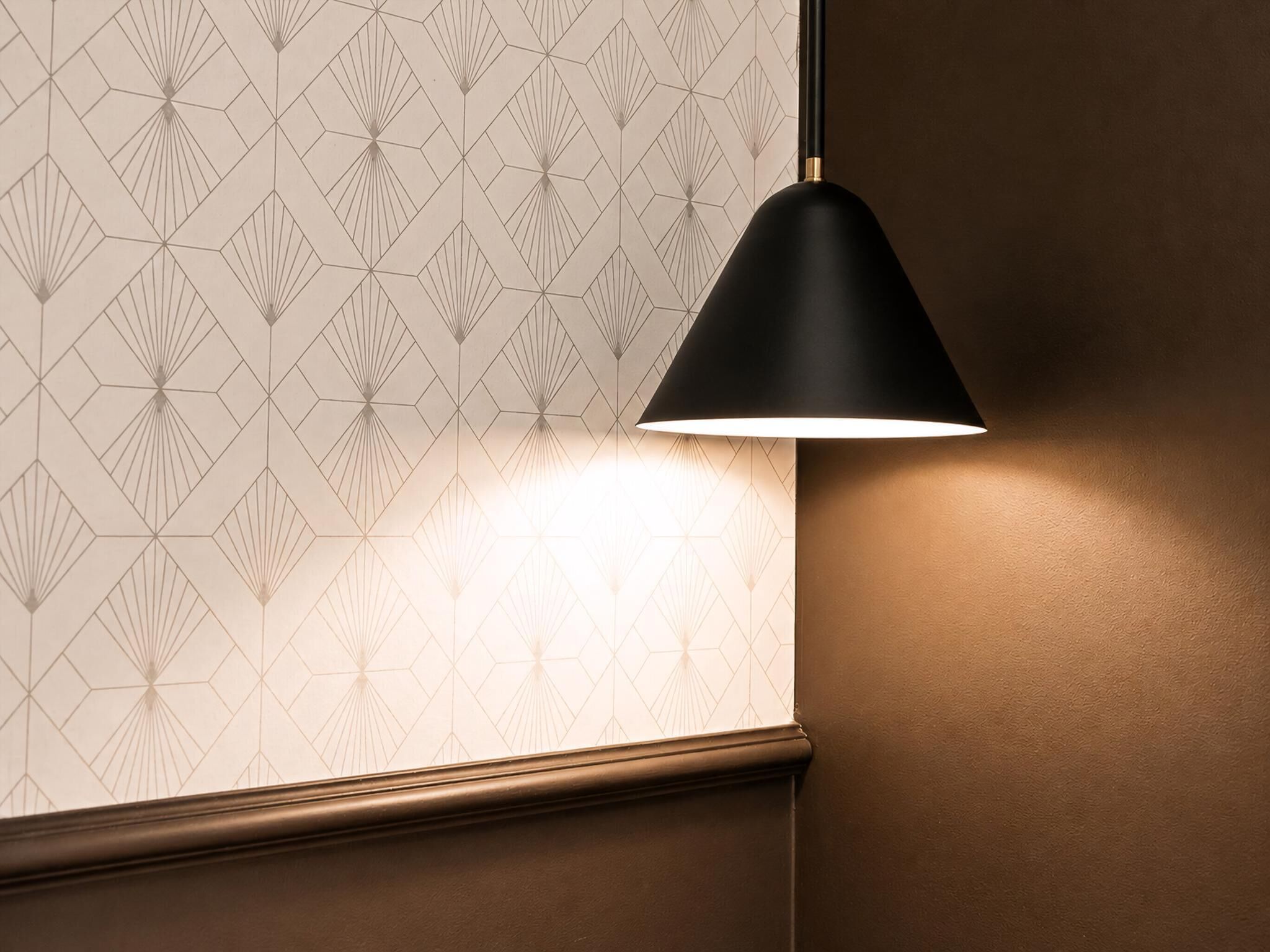 En væg med et geometrisk mønster og en hængende sort lampe.