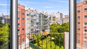 Un edificio residencial de varios pisos con balcones, unidades de aire acondicionado y una cerca verde.