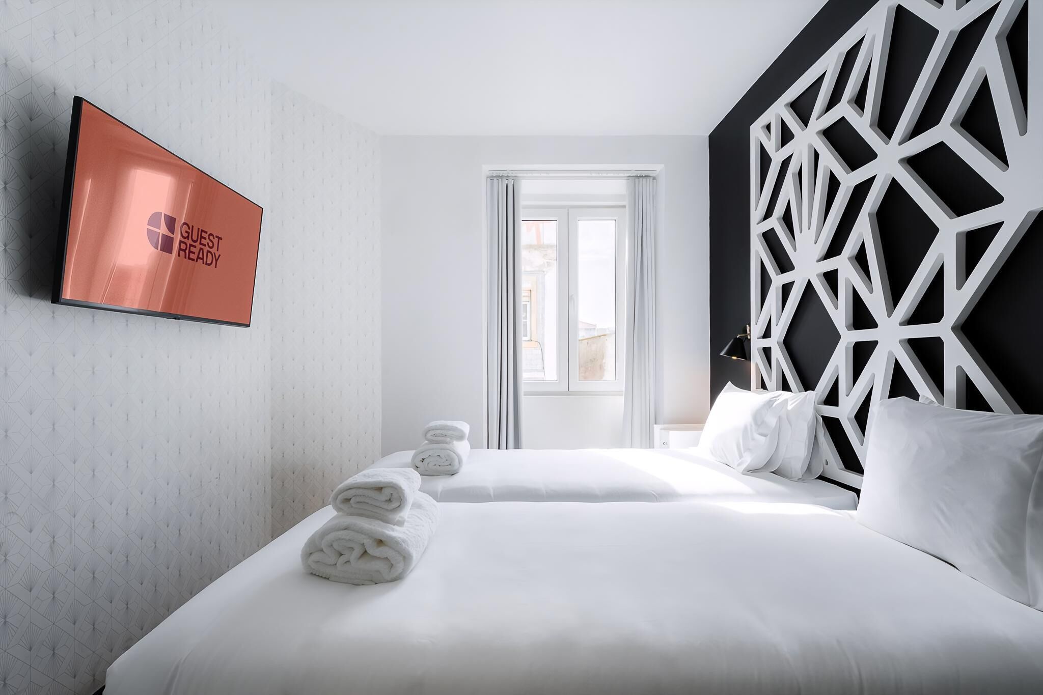 Ein Hotelzimmer mit Bett, Fernseher, geometrischem Wanddesign und Fenster.