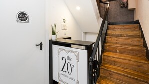 Una escalera con escalones de madera y barandas negras, una puerta blanca con un cartel que indica '04-05 Quartos' y un letrero en la pared que anuncia 'habitaciones y suites los años 20'.