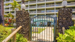 A hotel entrance with a gated driveway, a stone pillar with a sign, and a multi-story building with balconies in the background. - Stay Beachfront, Explore Maui’s Outdoors 629 LS (Lahaina)