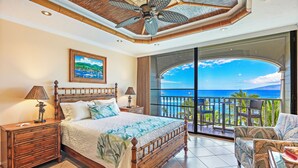 A bedroom with a large bed, wooden nightstands, a ceiling fan, and a balcony with a view of the ocean. - Stay Beachfront, Explore Maui’s Outdoors 629 LS (Lahaina)