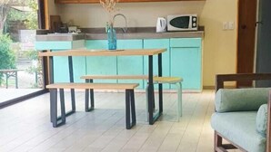 A modern kitchen with teal cabinets, a wooden dining table, and a built-in microwave. - Espacio Arenales (Paine)