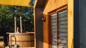 A wooden deck with a covered seating area, a wooden structure with a large window, and a yellow shade sail. - Espacio Arenales (Paine)
