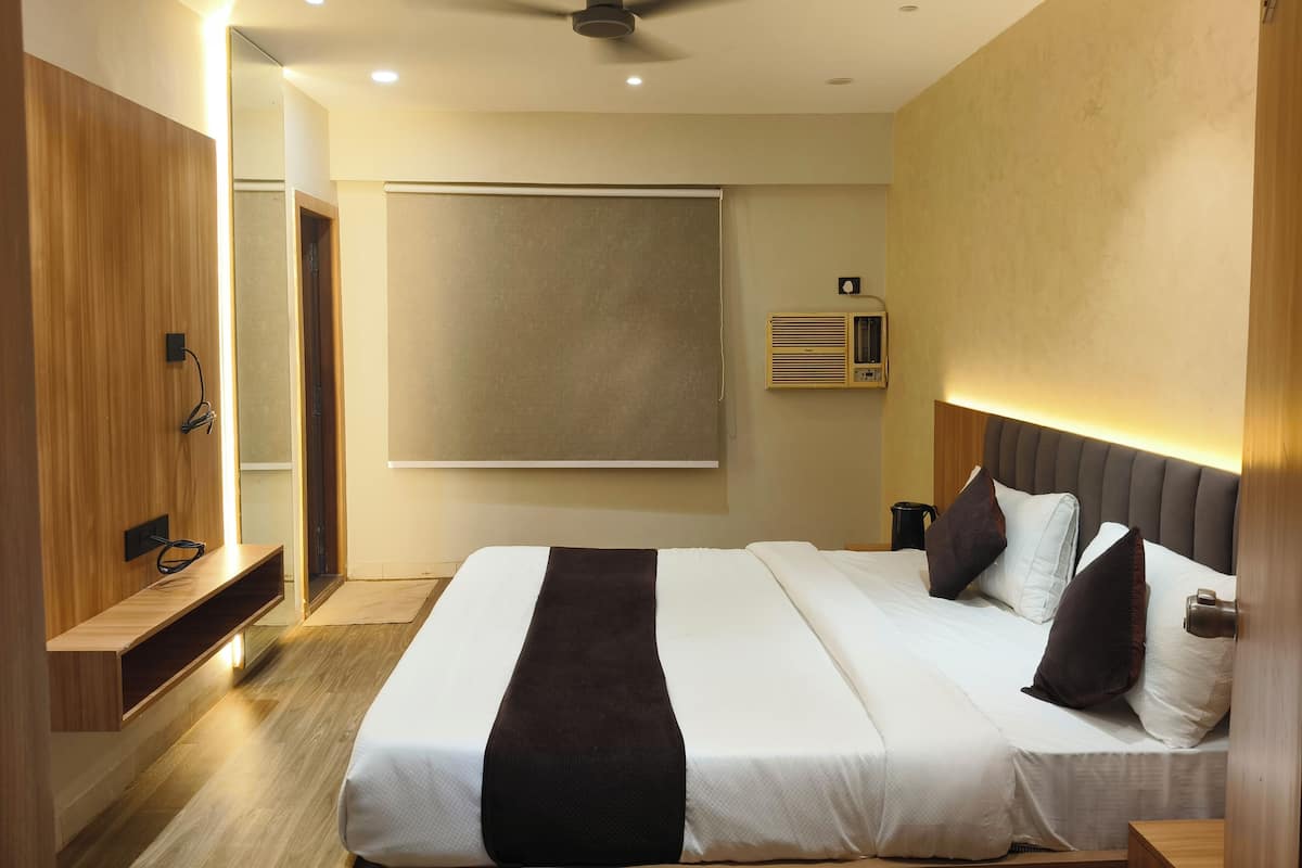 A modern hotel room with a large bed, a ceiling fan, a wall-mounted air conditioner, and a wooden bench.