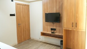 A room with a wooden wardrobe, a mounted TV, and a small shelf. - The samsara Hotel by Satyug (Ujjain)
