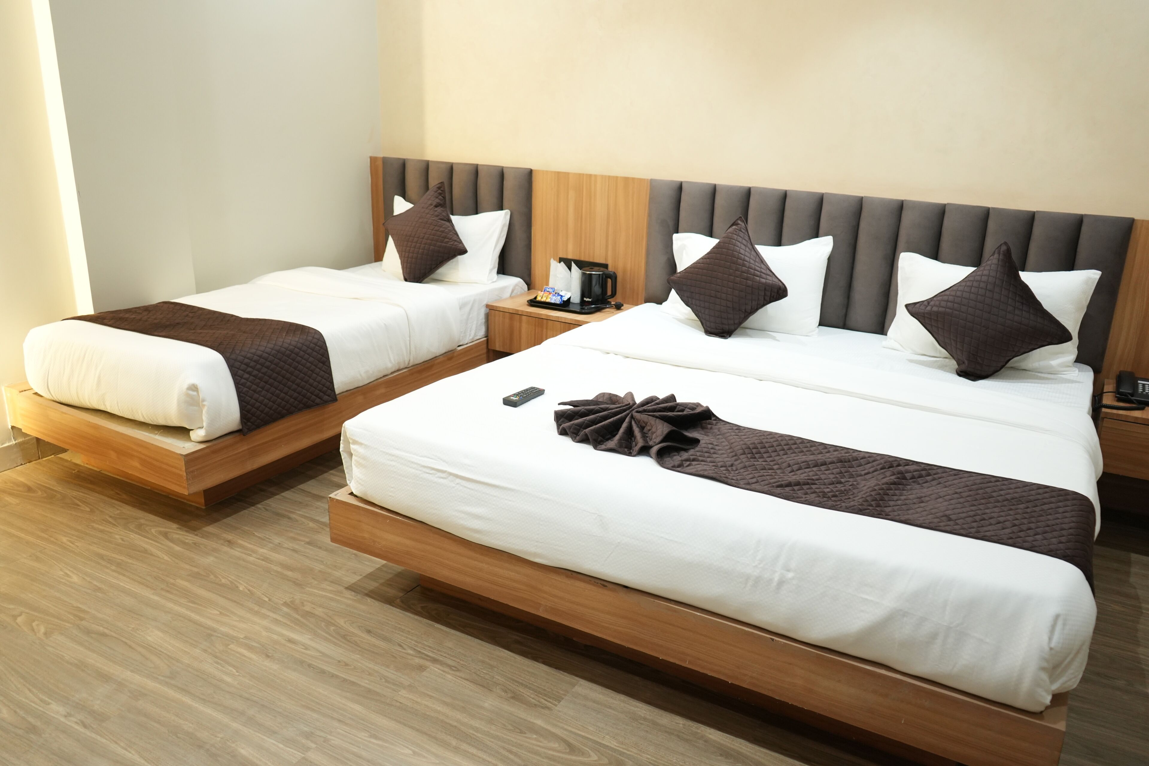 A hotel room with two single beds, wooden headboards, and a nightstand with a coffee maker.