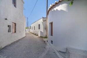 A narrow street with white buildings, small windows, and a clear sky.