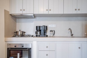 A kitchen with white cabinets, a stove, a coffee maker, and a sink.
