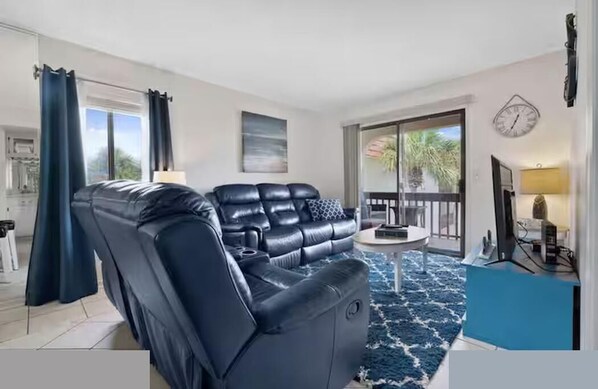A modern living room with a black leather sofa, a small round coffee table, and a blue rug. -  Escape with Private Beach Access & Coastal Charm (St. Augustine)