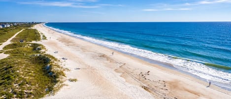 A beach with a clear sky, sandy shore, and a few people walking.