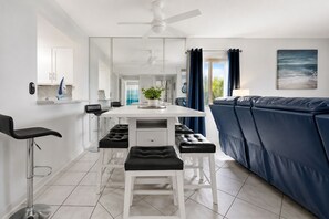 A modern kitchen with a dining area, a sofa, and a ceiling fan.