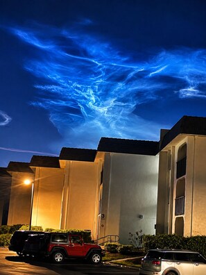 A building with a parking lot, two cars, and a clear sky with cloud formations.