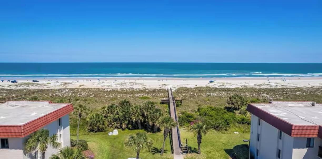 A beachfront property with two buildings, a paved walkway, and a parking area.