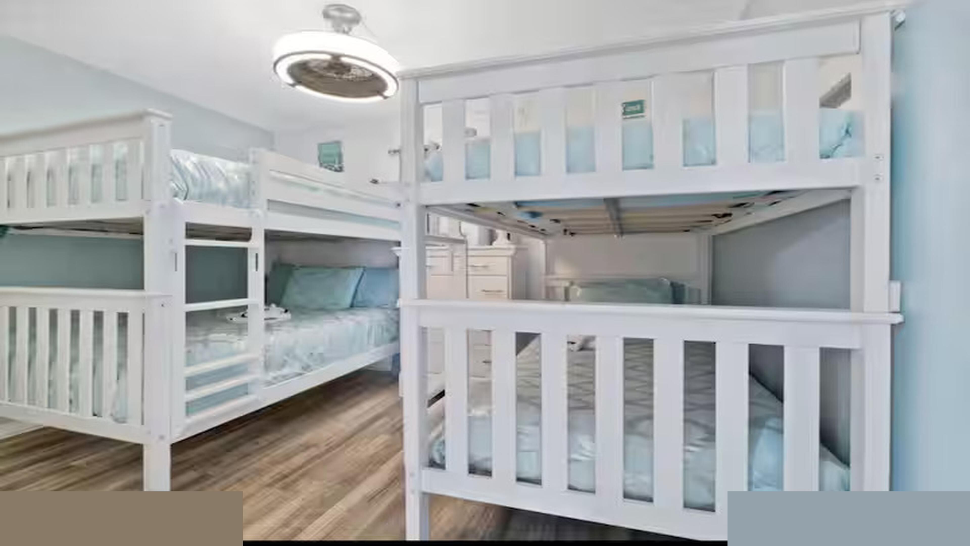 A room with bunk beds, a ceiling fan, and a small desk with drawers.