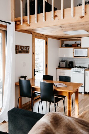 Een gezellig chaletinterieur met een houten eettafel, zwarte stoelen, een keuken met een magnetron en een bord waarop 'LAKE' staat.