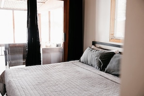 Een slaapkamer met een bed, een raam met jaloezieën en uitzicht op het balkon.