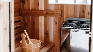 Una sauna de madera con un banco, un balde de madera y un calentador de sauna marcado con el nombre HARVIA.