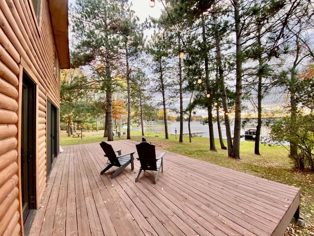 Una terraza de madera con dos sillas, con vistas a un lago, árboles y un muelle al fondo.