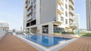 Ein modernes Apartmenthaus mit Pool auf dem Dach, Balkonen und blauem Himmel.