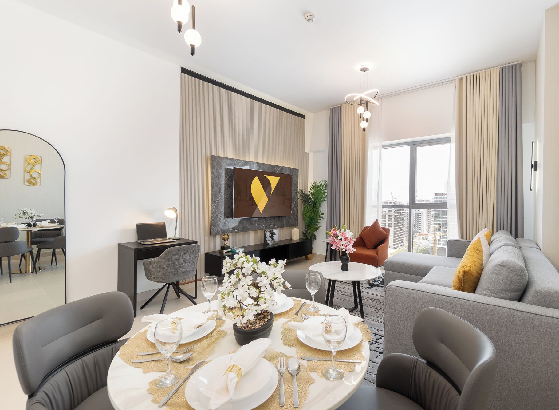 Una sala de estar moderna con un sofá gris, una mesa de comedor preparada para cuatro personas y un televisor de pantalla plana montado en la pared.