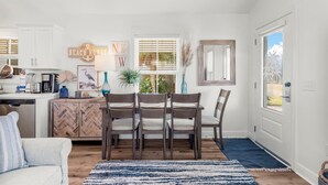 A bright kitchen with white cabinets, a wooden herringbone cabinet, a dining table with four chairs, and a blue rug. - Beach House - Sun-kissed Cottage by PHG (Port St. Joe)