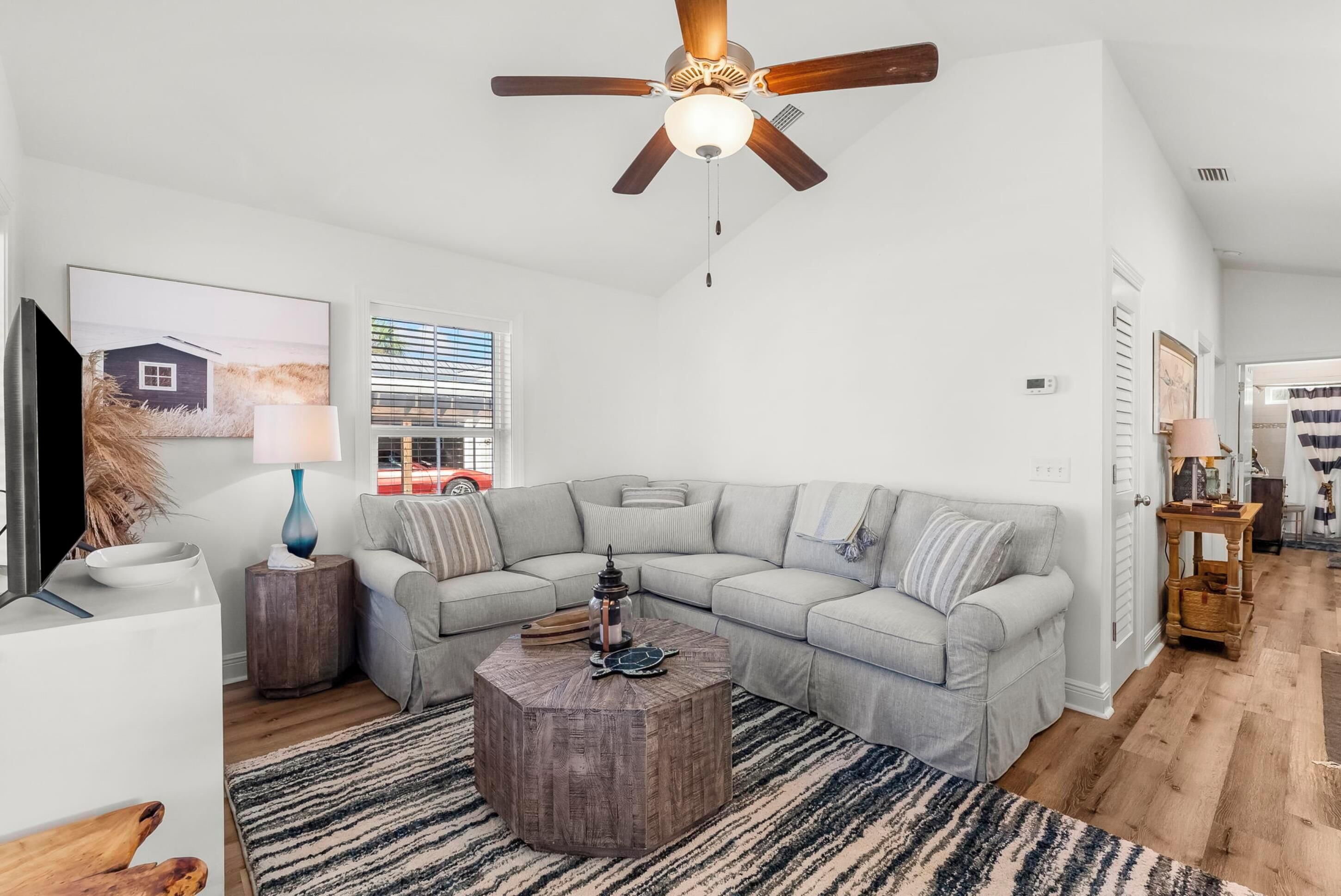 A living room with a sectional sofa, a wooden coffee table, a ceiling fan, and a window with blinds.