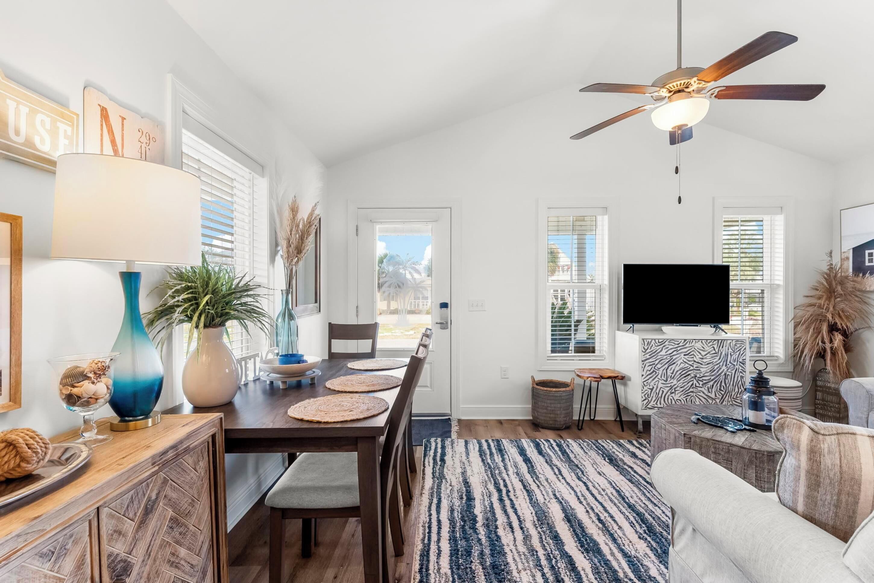 A spacious living room with a dining area, a ceiling fan, a television, and a large window.