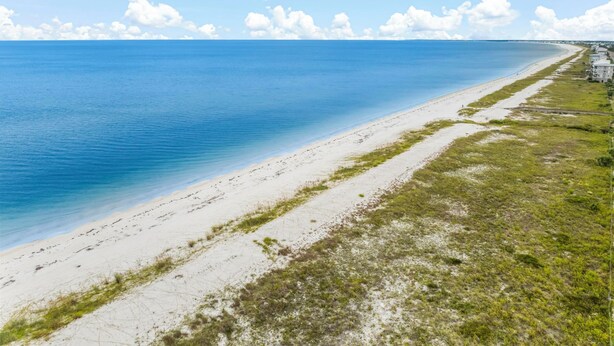 A beach with a clear blue sea, sandy shore, and a few buildings in the distance. - Beach House - Sun-kissed Cottage by PHG (Port St. Joe)