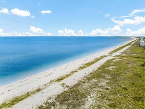 A beach with a clear blue sea, sandy shore, and a few buildings in the distance. - Beach House - Sun-kissed Cottage by PHG (Port St. Joe)