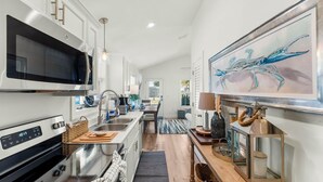 A modern kitchen with stainless steel appliances, a dining area with a view, and a large painting on the wall. - Beach House - Sun-kissed Cottage by PHG (Port St. Joe)